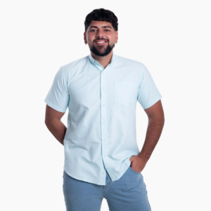 Hombre sonriente luciendo camisa de manga corta azul claro con cuello cubano y bolsillo.