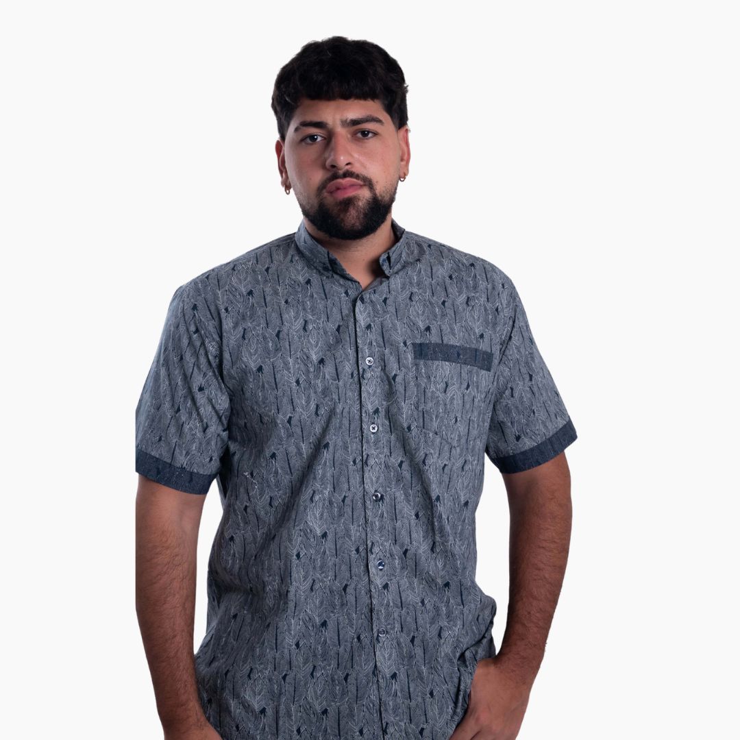 Un modelo posando con una camisa de manga corta para hombre con un patrón de estampado gráfico gris oscuro sobre un fondo blanco.